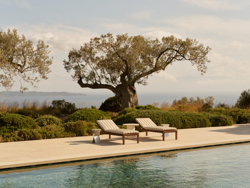 Lounge chairs by a pool at Amanzoe, Greece, with an olive tree and sea view in the background.