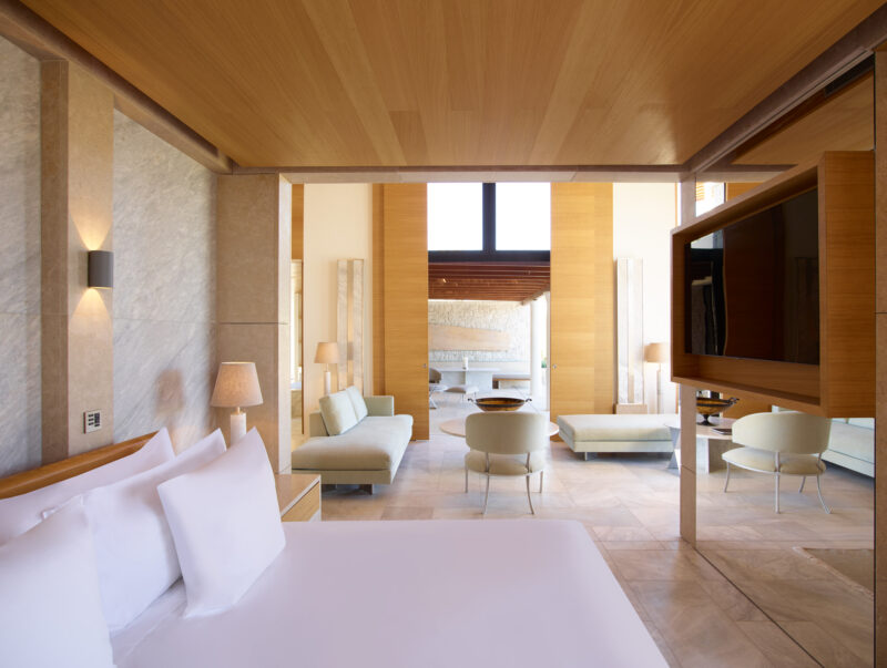 Luxurious bedroom in Villa 18 at Amanzoe, featuring modern decor, a large bed, and a view into a spacious living area.