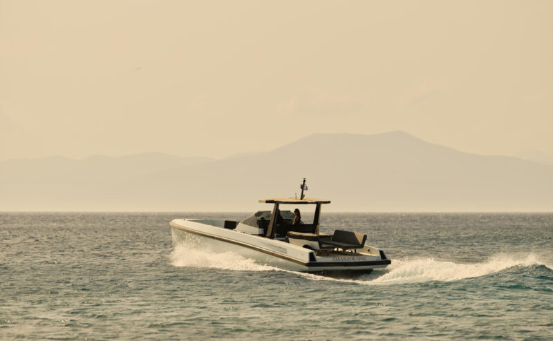 Powerboat named "Amanzoe" cruising on calm waters with mountains in the background, under a hazy sky.
