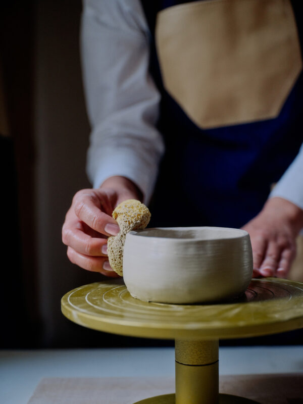 Hand applying a sponge to a freshly shaped ceramic bowl on a pottery wheel during an art class at Amanzoe, Greece.