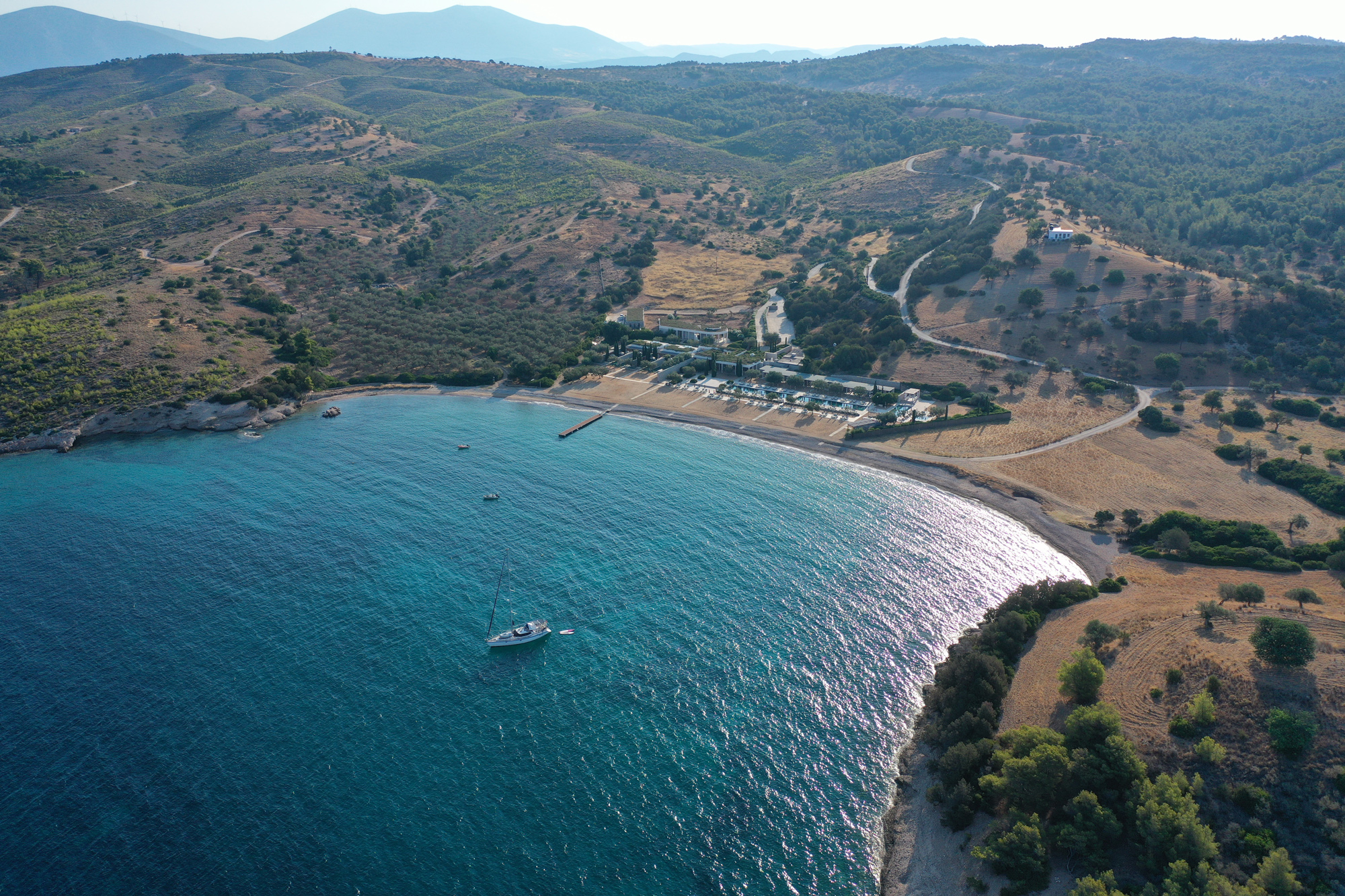 Aerial view of a serene beach in Amanzoe, Greece, with hills and a sailboat in the turquoise water, July 2022.