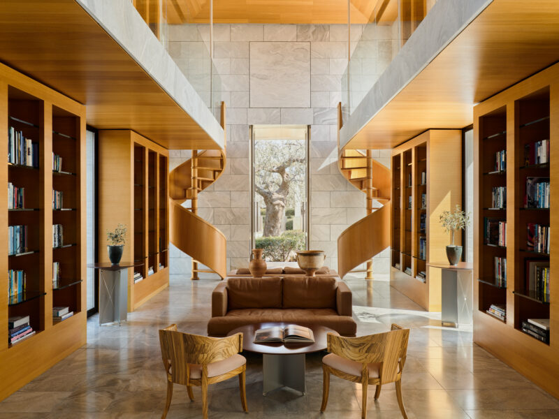 Modern library interior at Amanzoe Resort, featuring wooden shelves, a cozy seating area, and large windows overlooking gr...