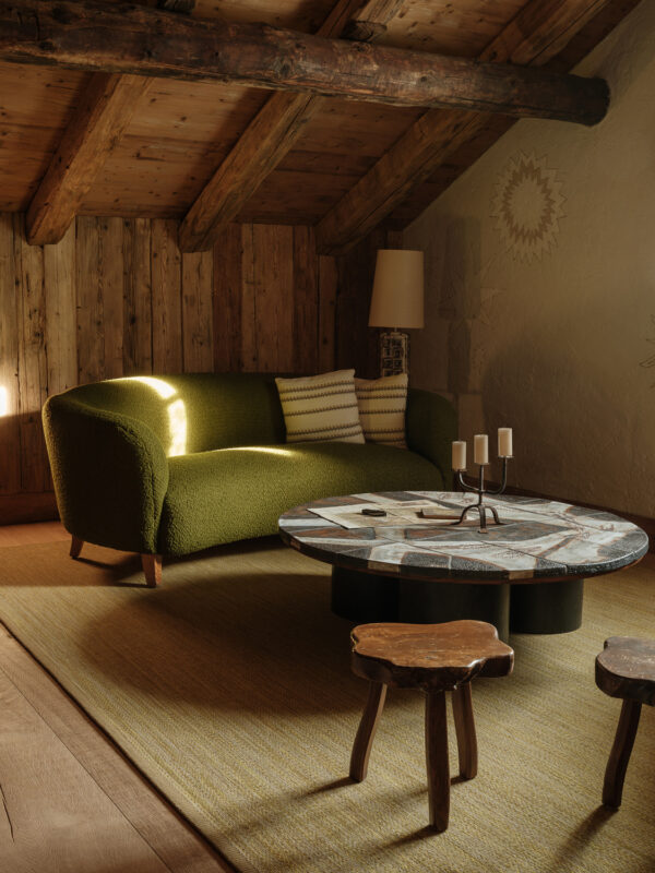 Cozy interior of a rustic room featuring a green sofa, a round coffee table, and wooden stools under a wooden ceiling.