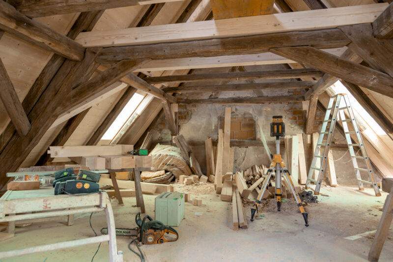 Renovation in an attic with wooden beams, tools, and construction materials scattered around.