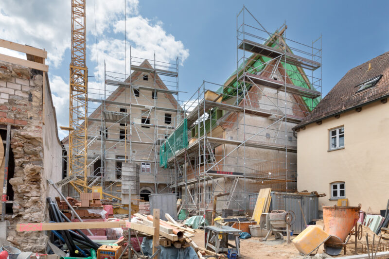 Construction site with scaffolding around a partially built building, surrounded by construction materials and equipment.