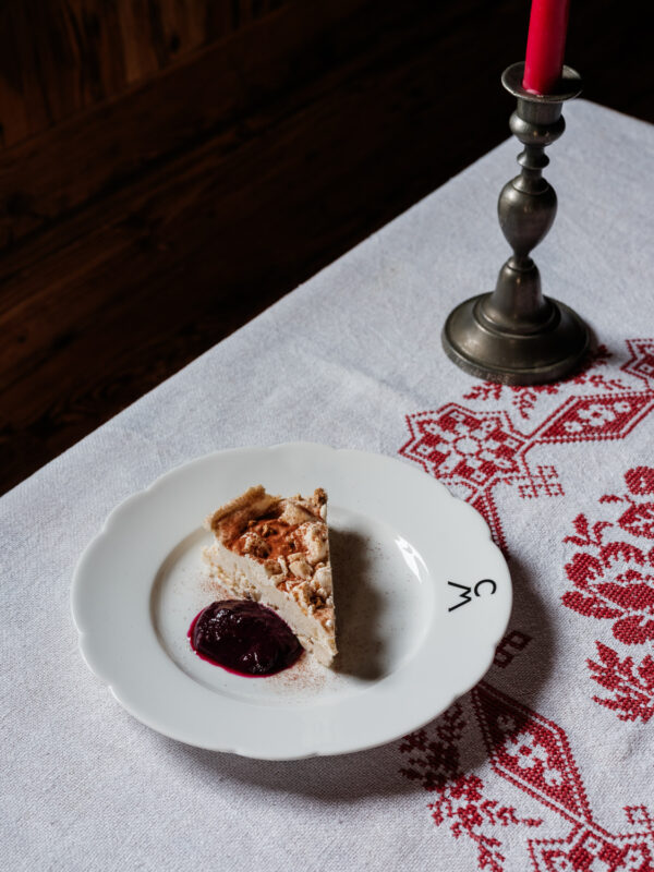 Slice of chestnut semifreddo on a decorative plate with berry sauce, set on a table with a red candle and embroidered tabl...