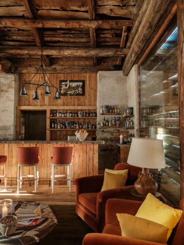 Cozy cocktail bar lounge with wooden beams, a stocked bar, and orange armchairs, featuring warm lighting and decor.