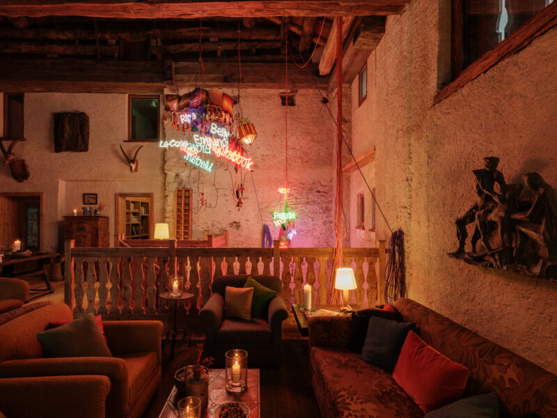 Cozy lounge area in Chesa Marchetta with colorful neon signs, rustic decor, and comfortable seating.