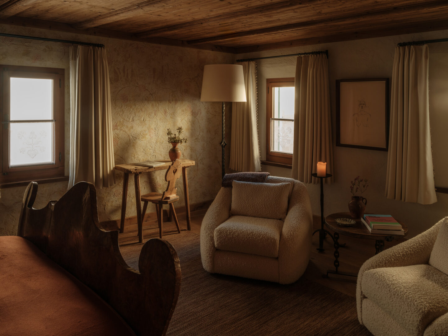 Cozy interior of a winter cabin featuring a plush armchair, wooden table, and warm lighting from a lamp and candle.