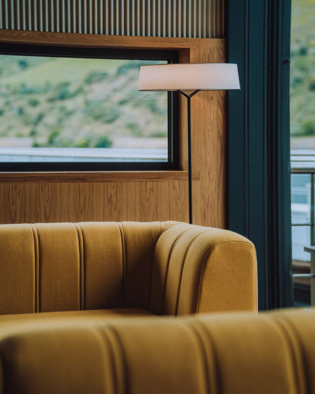 Cozy interior featuring a yellow upholstered sofa and a modern floor lamp beside a large window with a scenic view.