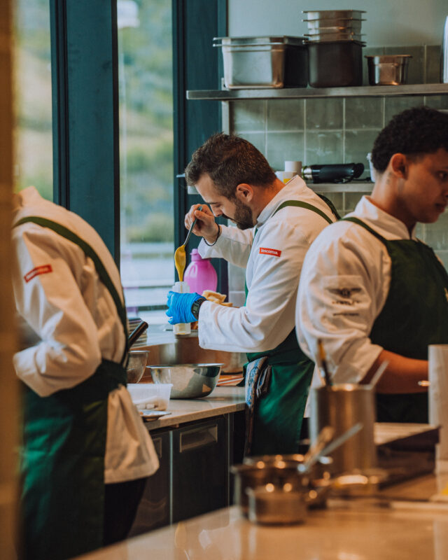 Chefs in a modern kitchen preparing food, focused on their tasks with various utensils and ingredients.
