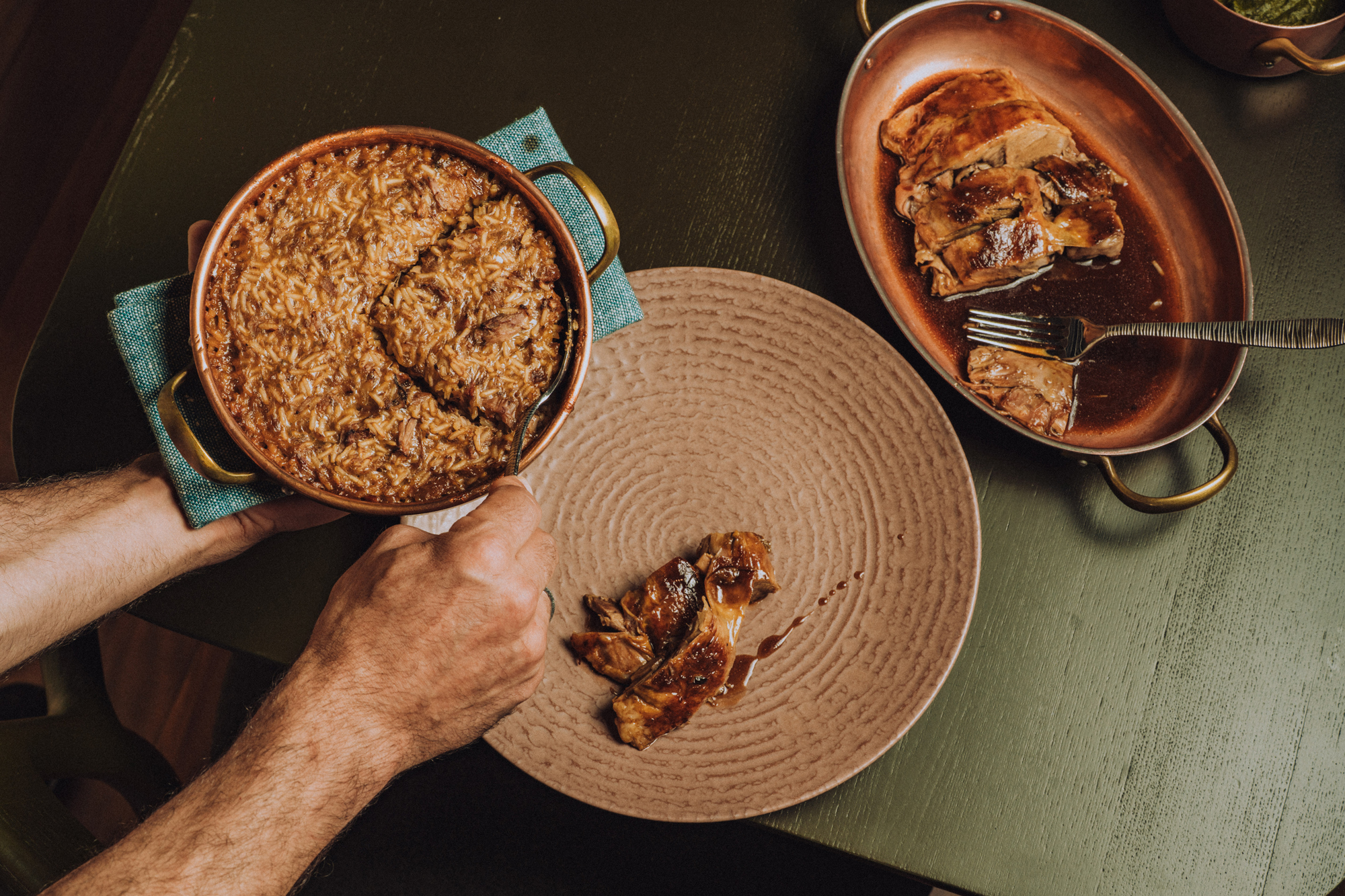 A person serving rice from a pot onto a textured plate, with sliced meat and sauce on a separate dish.