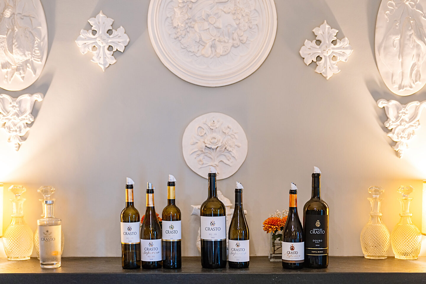 Bottles of Quinta do Crasto wine displayed on a shelf, with decorative wall elements and soft lighting in the background.