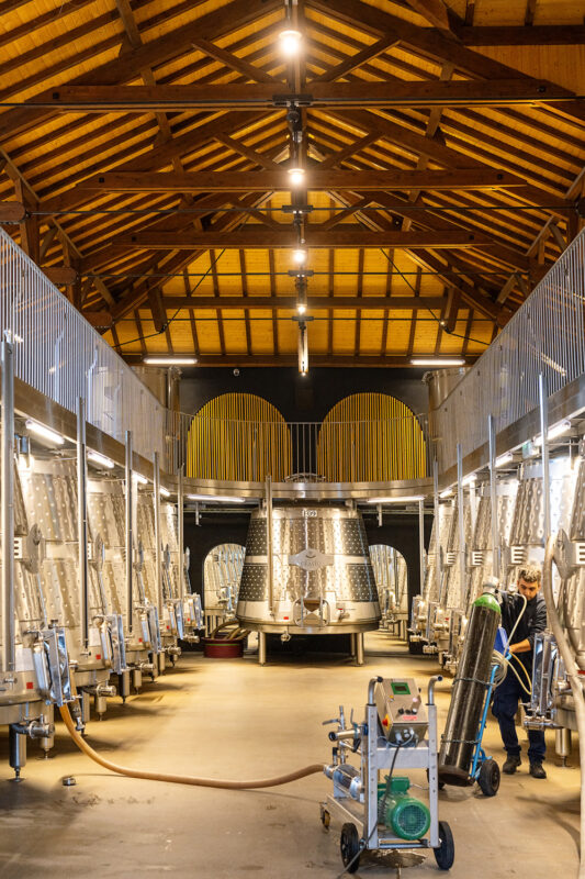 Modern wine cellar with stainless steel fermentation tanks and a worker using equipment in Quinta do Crasto.