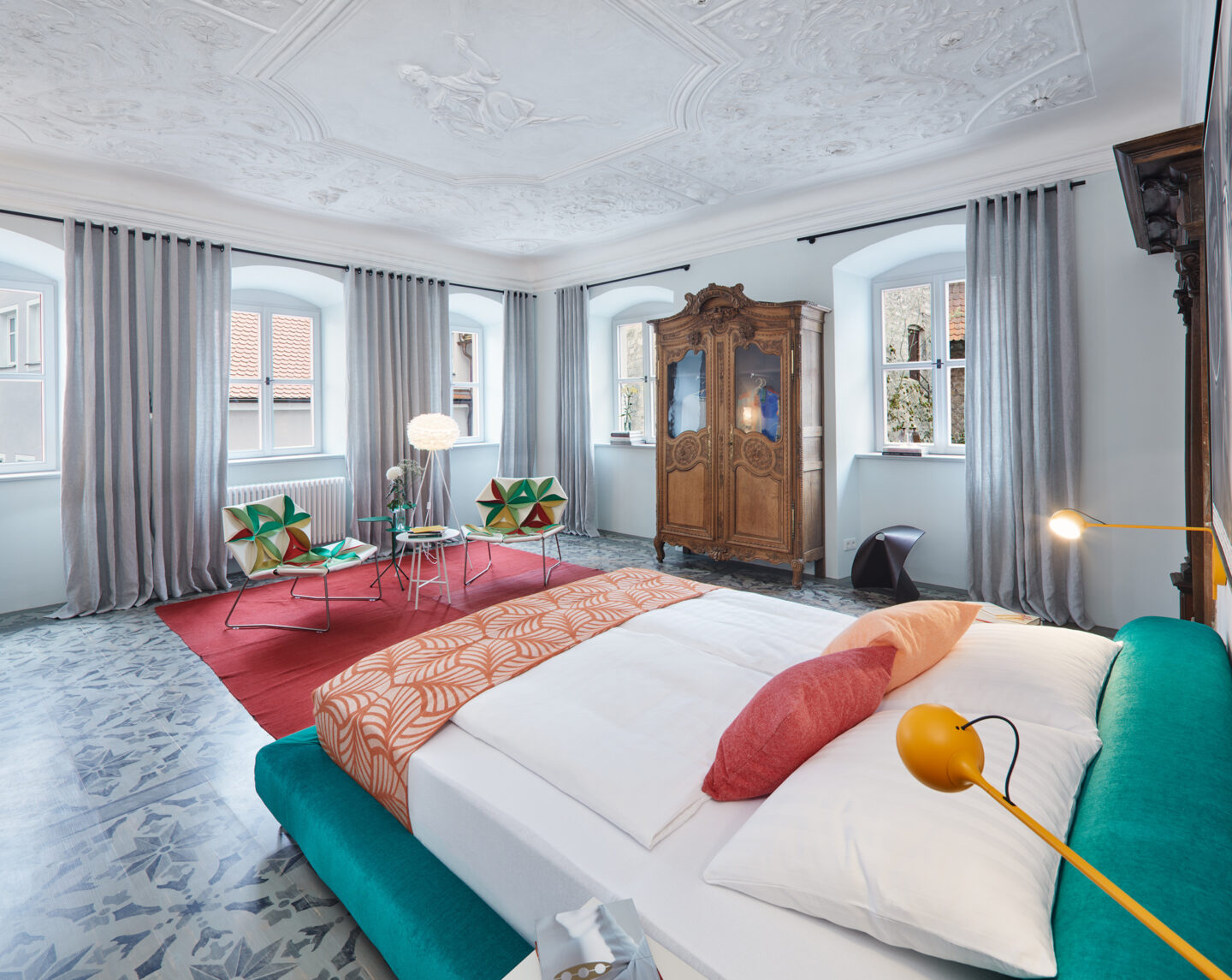 Stylish apartment interior featuring a bed, vintage wardrobe, modern chairs, and ornate ceiling details.