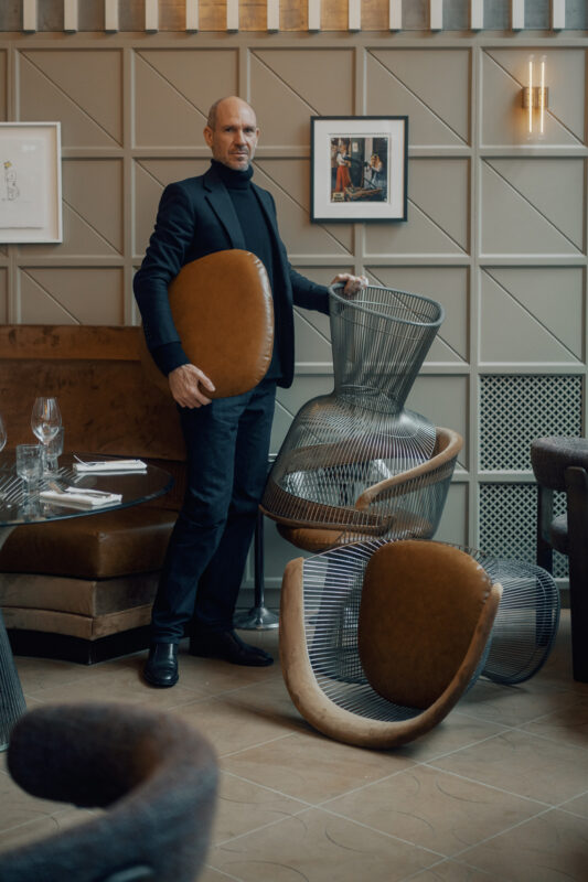 Man holding a round cushion stands among modern furniture in a stylish restaurant interior.