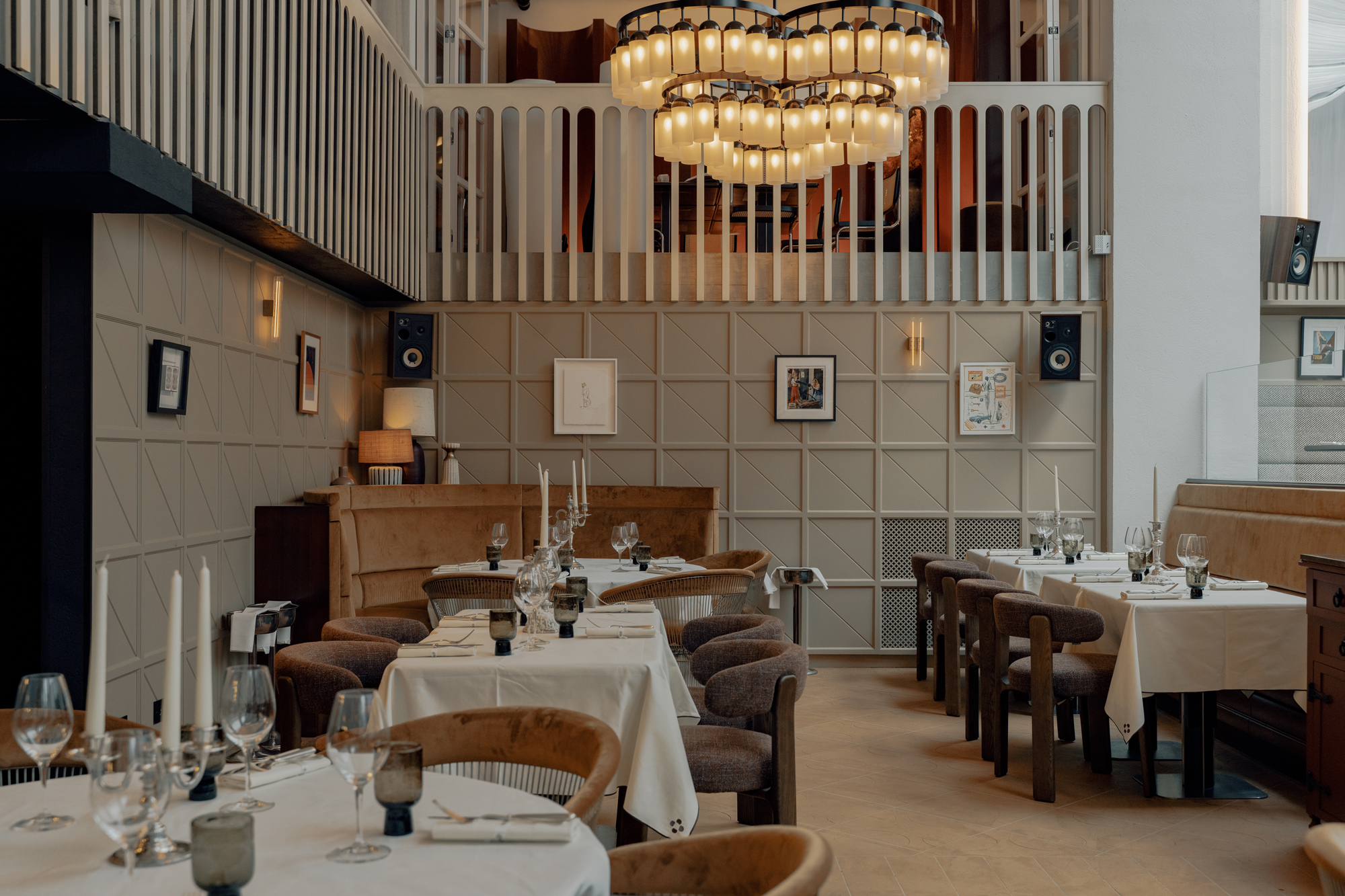 Elegant restaurant interior featuring round tables set with white tablecloths, candles, and a large chandelier overhead.