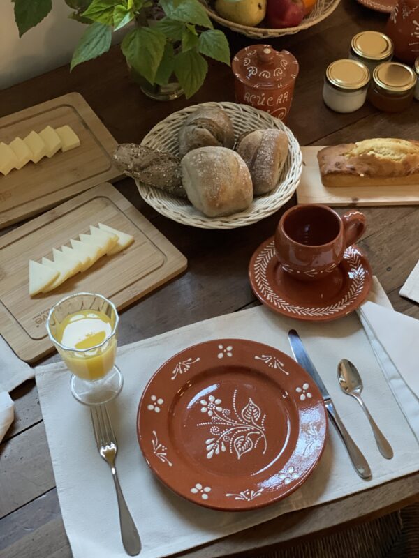 Rustic breakfast setting with a decorated plate, glass of orange juice, bread rolls, cheese, and a clay mug on a wooden ta...