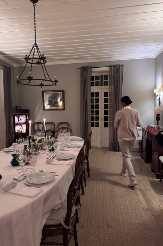 Elegant dining room at Quinta do Crasto, featuring a long table set with glassware and a woman walking towards a sideboard.