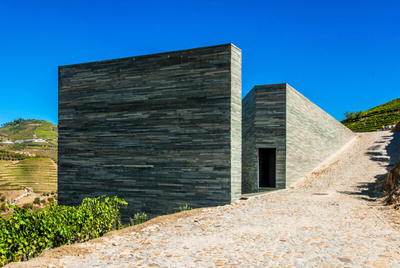 Modern stone building at Quinta do Vallado, surrounded by vineyards and clear blue sky.