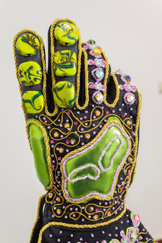 Colorful, intricately designed glove featuring green and yellow elements, embellished with beads and decorative stitching.