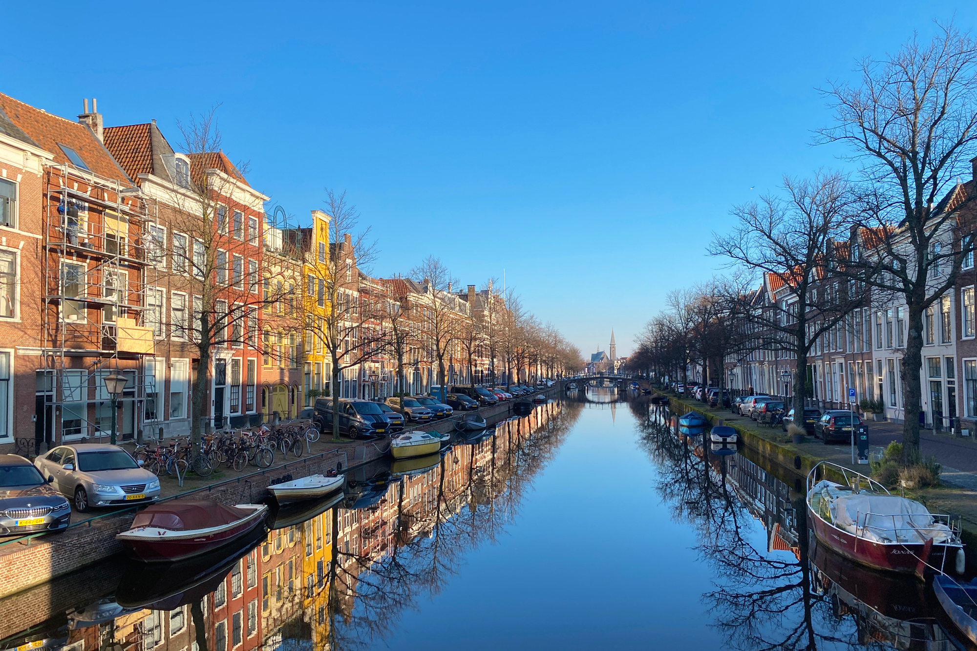 Canal view in Leiden with colorful boats and historic buildings reflecting in the water under a clear blue sky.