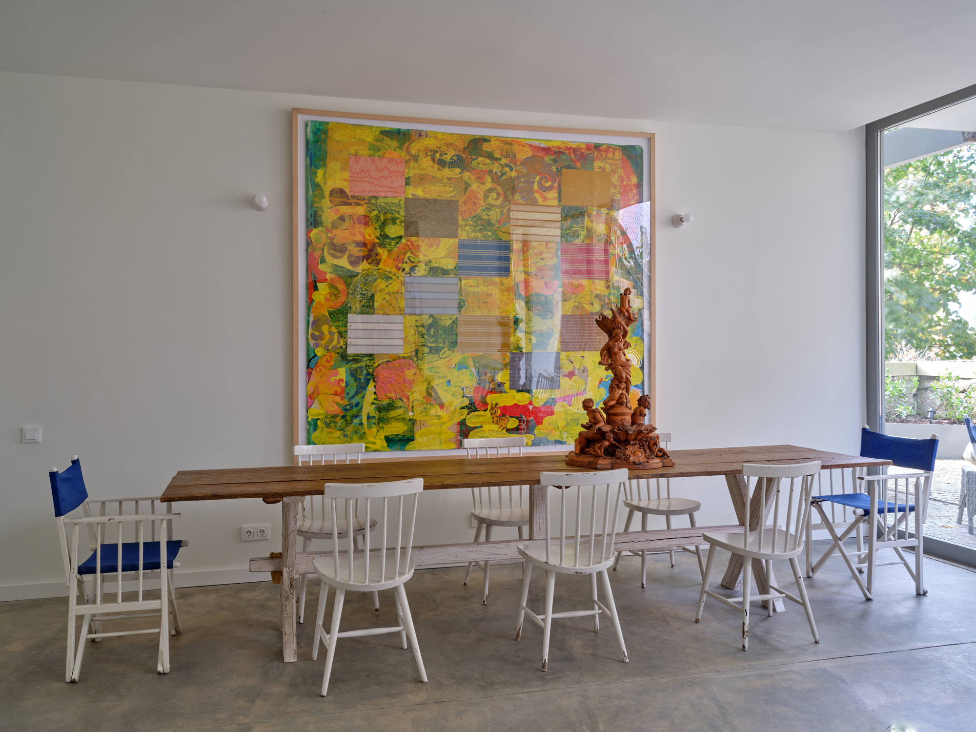 Brightly colored abstract artwork hangs on a white wall above a wooden table surrounded by white chairs in a modern cafete...