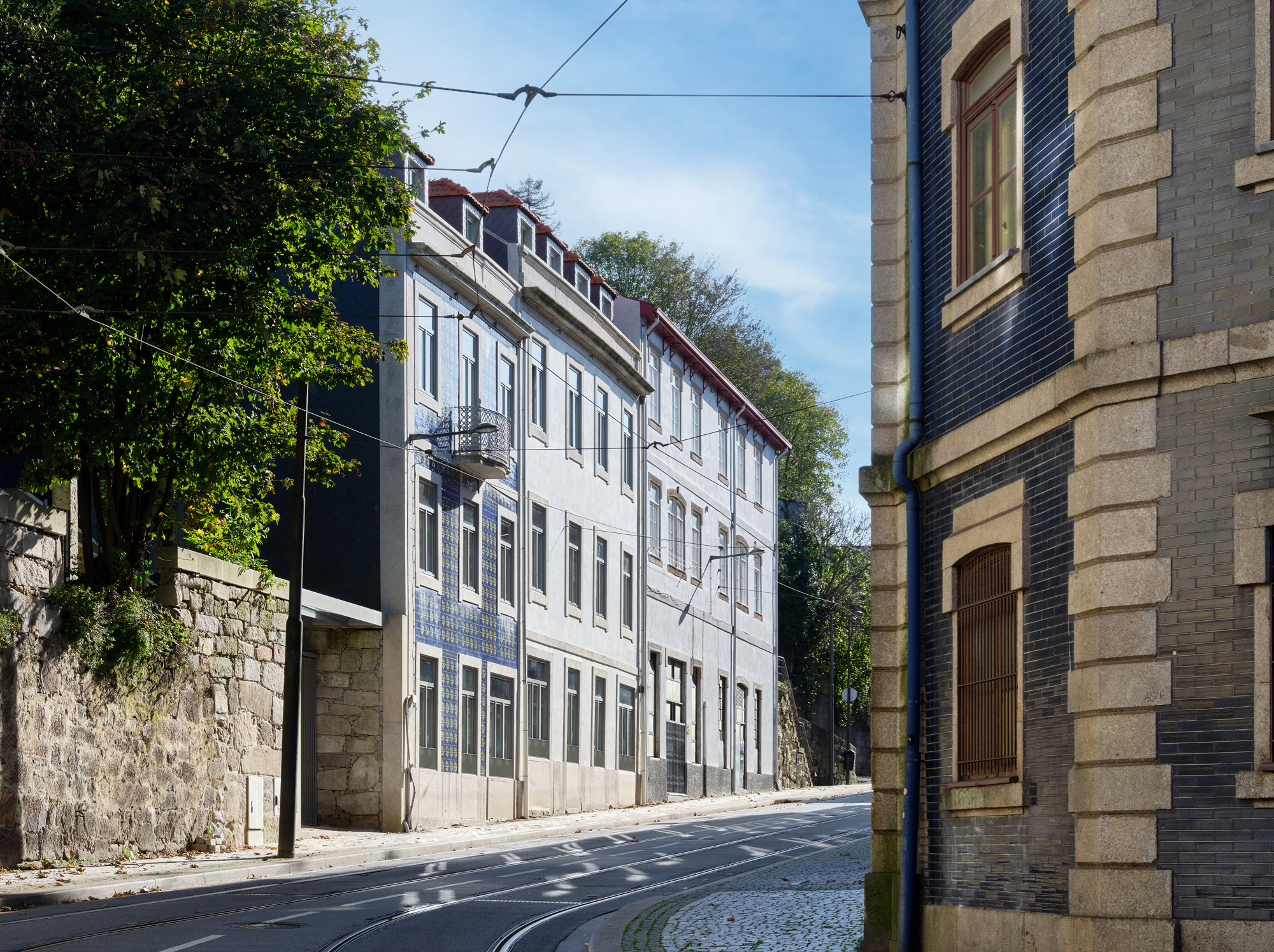 Historic buildings along a quiet street, featuring a mix of stone and modern facades under a clear blue sky.