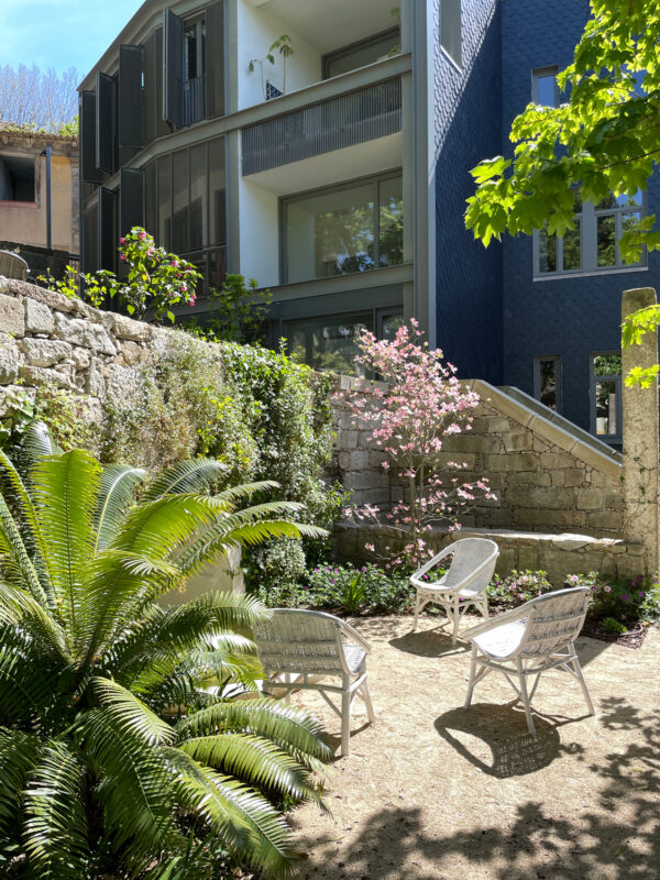 Gardens with white chairs, a flowering tree, and lush greenery beside a modern building at Massarelos House.