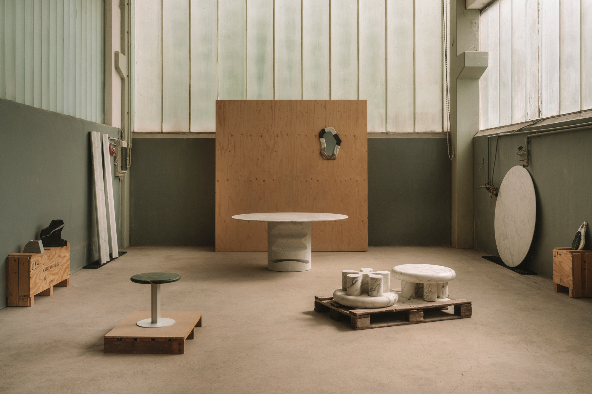Minimalist interior showcasing various sculptural furniture pieces, including a round table and pedestal, against a light-...