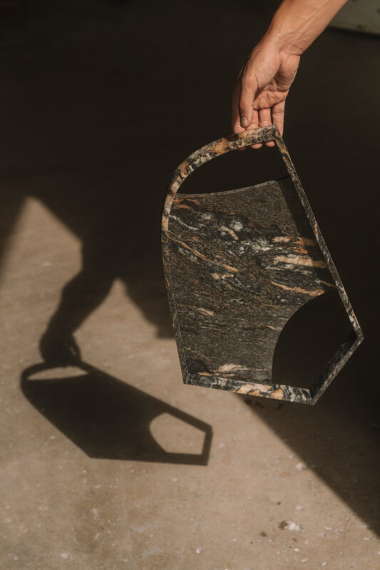 Hand holding a marbled stone tray, casting a distinct shadow on a textured surface.