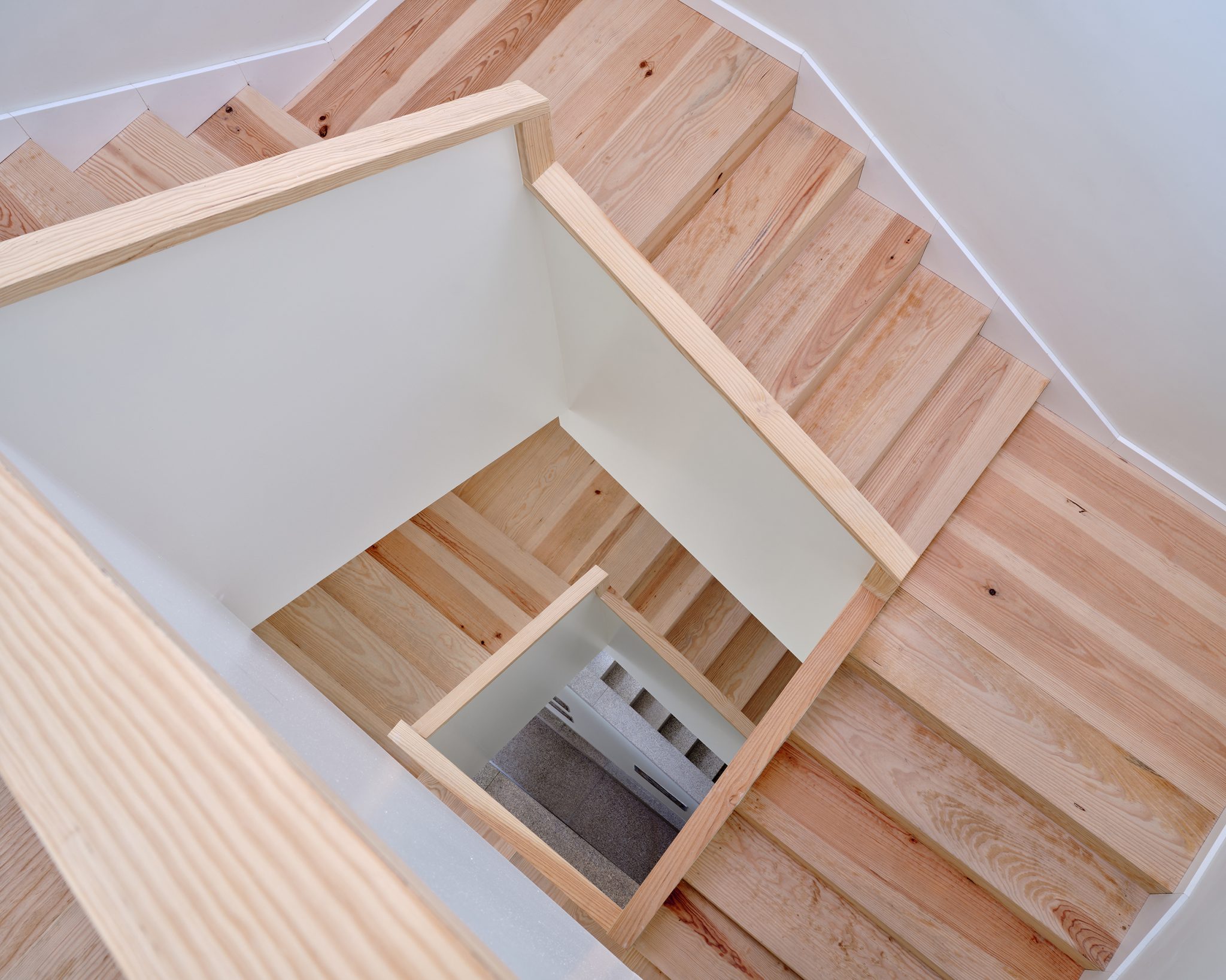 Wooden staircase with light-colored steps and a white railing, viewed from above, inside Massarelos House, Porto.