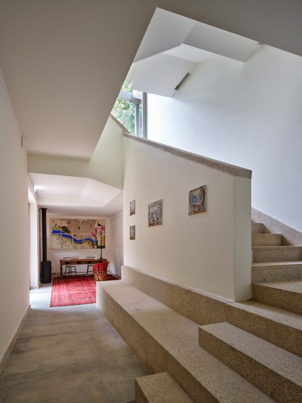 Bright, modern interior of Massarelos House featuring a staircase, artwork on the wall, and a view into a room with a red ...