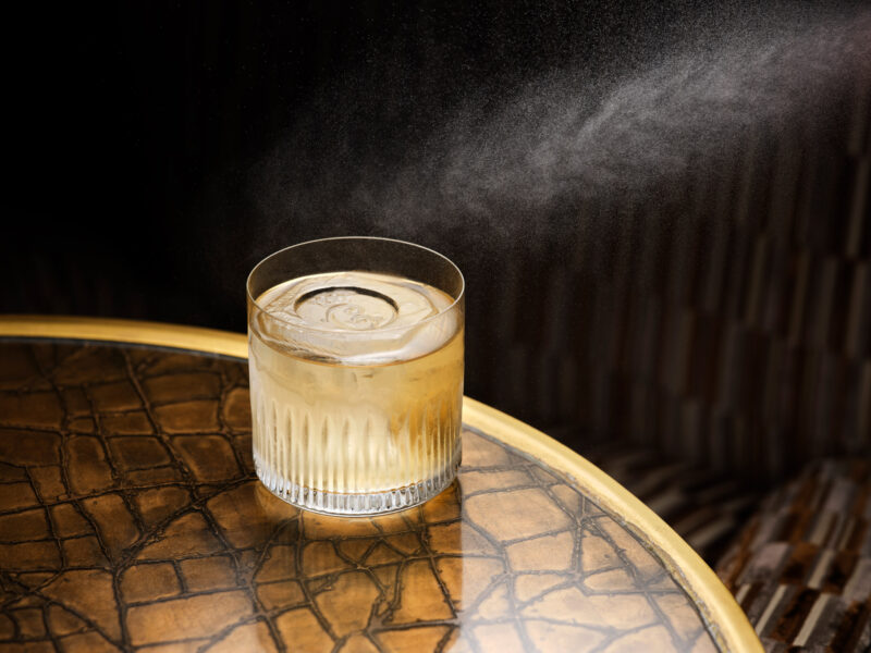 Glass of cocktail on a textured table, with a subtle mist in the background, evoking a serene atmosphere.