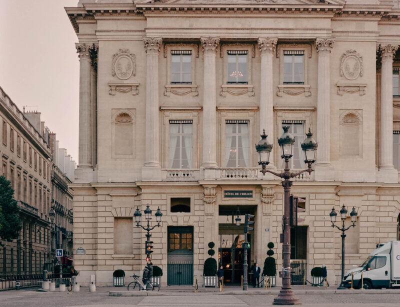 Facade of Hôtel de Crillon with ornate architecture, street lamps, and a glimpse of the entrance.