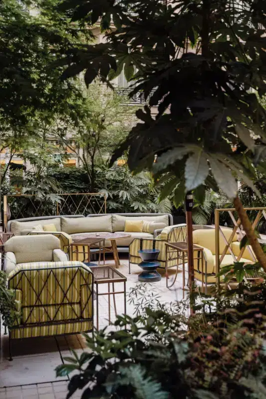Lush courtyard at Hôtel de Crillon featuring yellow and green seating among tropical plants.