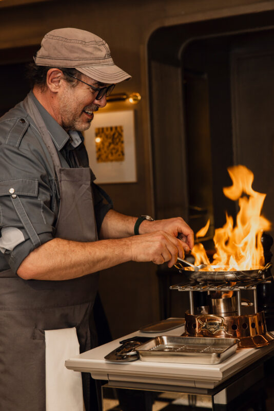 Chef Paul Pairet prepares a flaming pepper steak at Hôtel de Crillon's restaurant, showcasing culinary expertise.