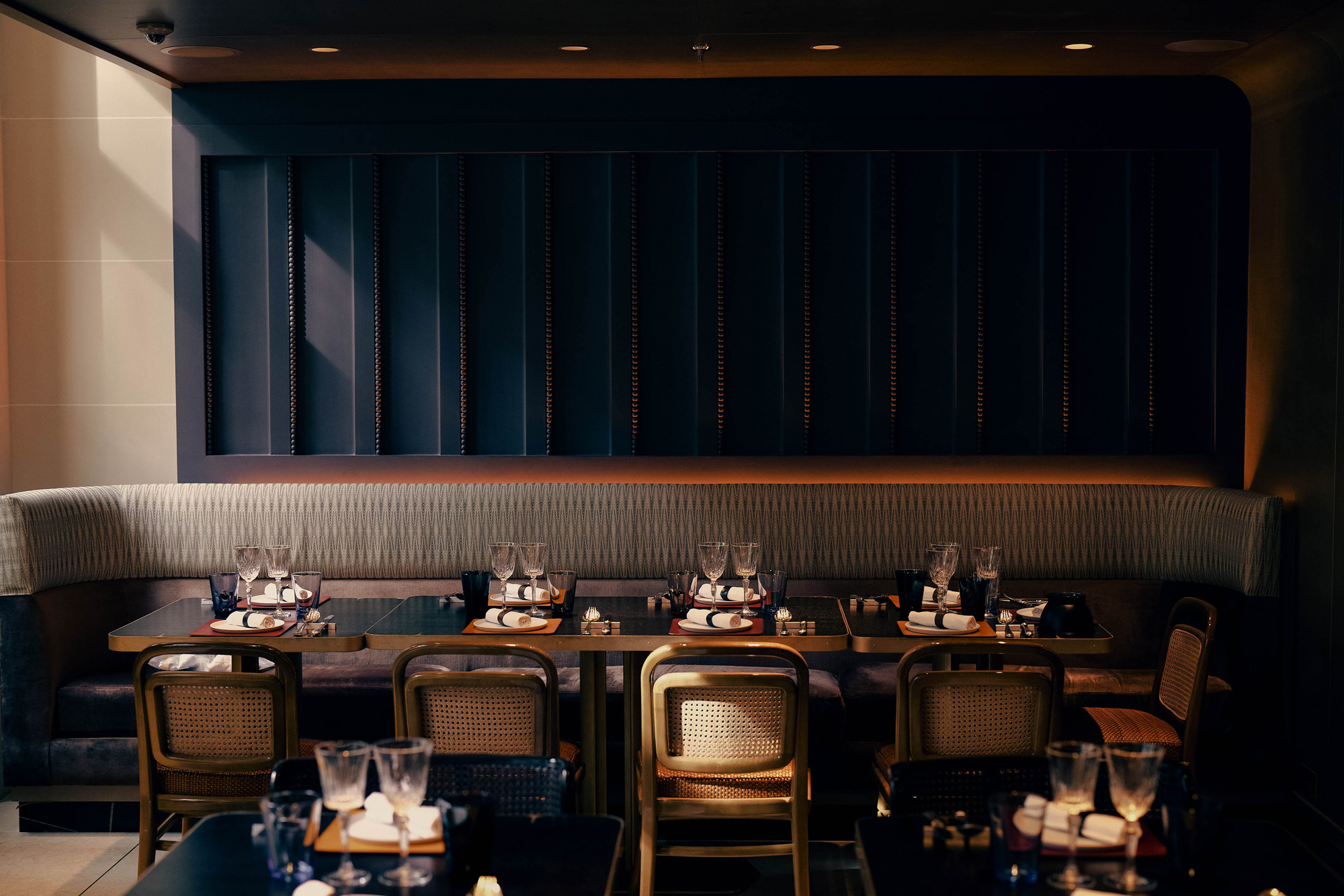 Elegant restaurant interior with a curved banquette, wooden tables set for dining, and soft lighting.