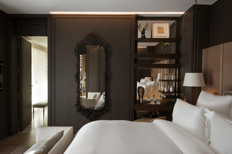 Elegant hotel bedroom featuring a large mirror, plush bedding, and stylish decor in dark wood tones.