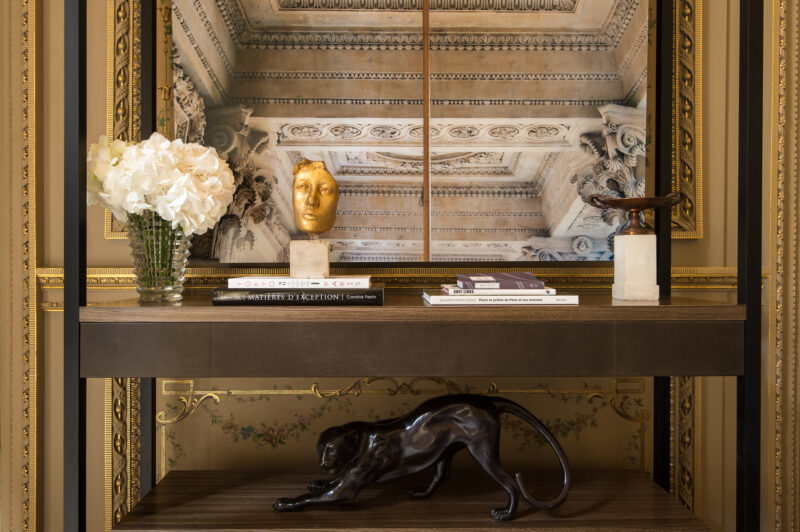 Elegant living room detail from Hôtel de Crillon featuring a decorative console, sculptures, and floral arrangement.