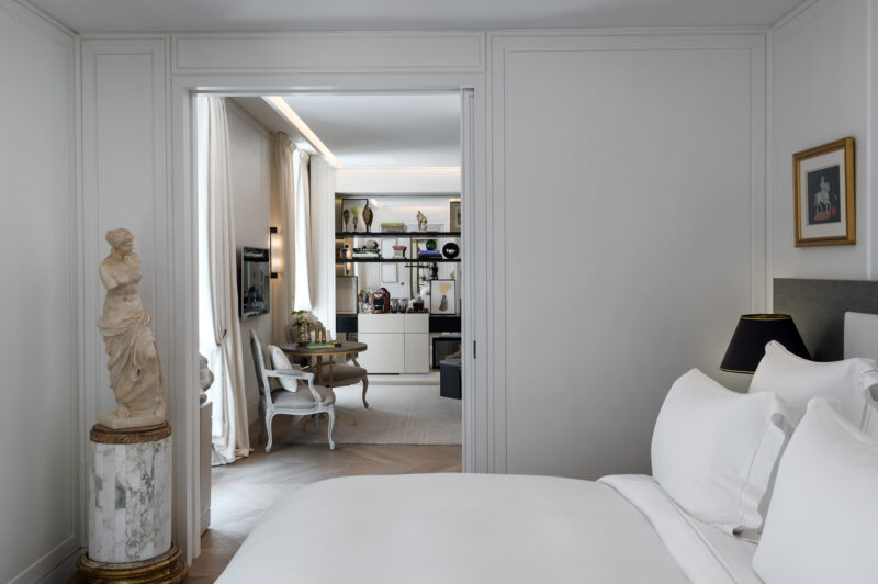 Elegant hotel suite featuring a bedroom with a marble statue, leading to a stylish living area with modern decor.