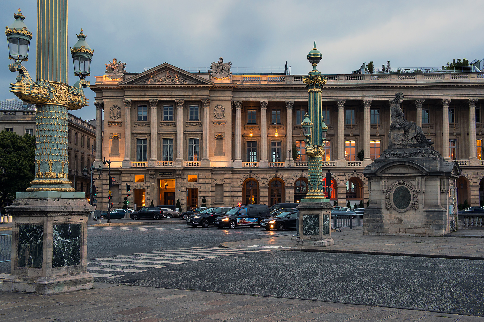 Hôtel de Crillon facade illuminated at night, with street lamps and a statue in the foreground.