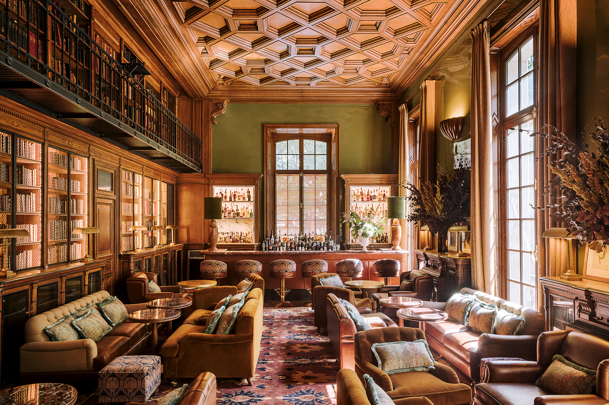 Elegant library bar with wooden paneling, plush seating, and a well-stocked bar, bathed in natural light.