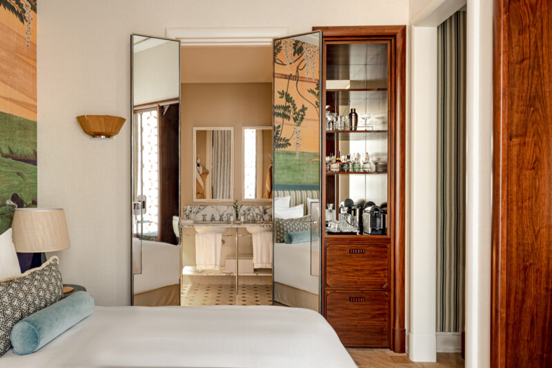 Elegant hotel boudoir featuring a bed, mirrored wardrobe, and a view of the bathroom with vintage decor.
