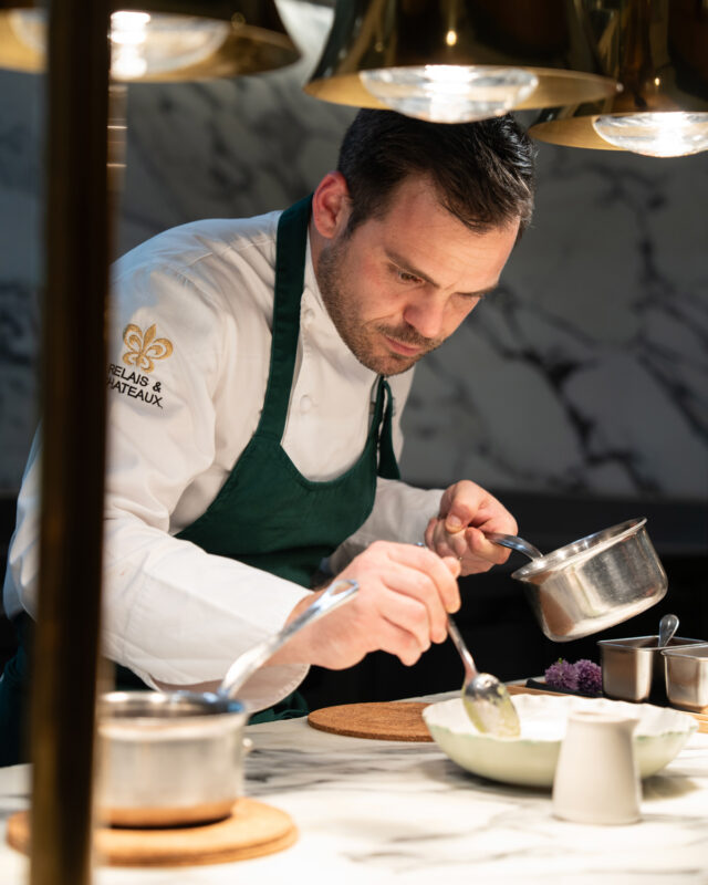 Chef Grégory Garimbay meticulously prepares a dish in the kitchen of Saint James Paris, surrounded by elegant lighting.