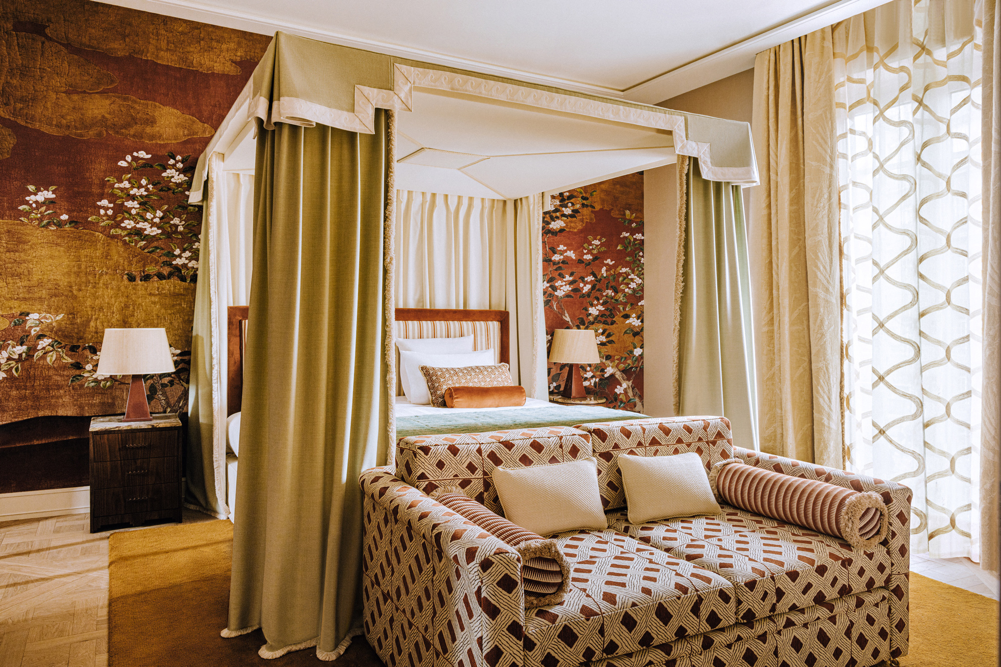 Luxurious hotel room featuring a four-poster bed, floral wallpaper, and a cozy seating area with patterned upholstery.