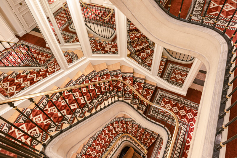 Elegant mirror staircase with intricate patterned carpet and ornate railings at Saint James Paris.