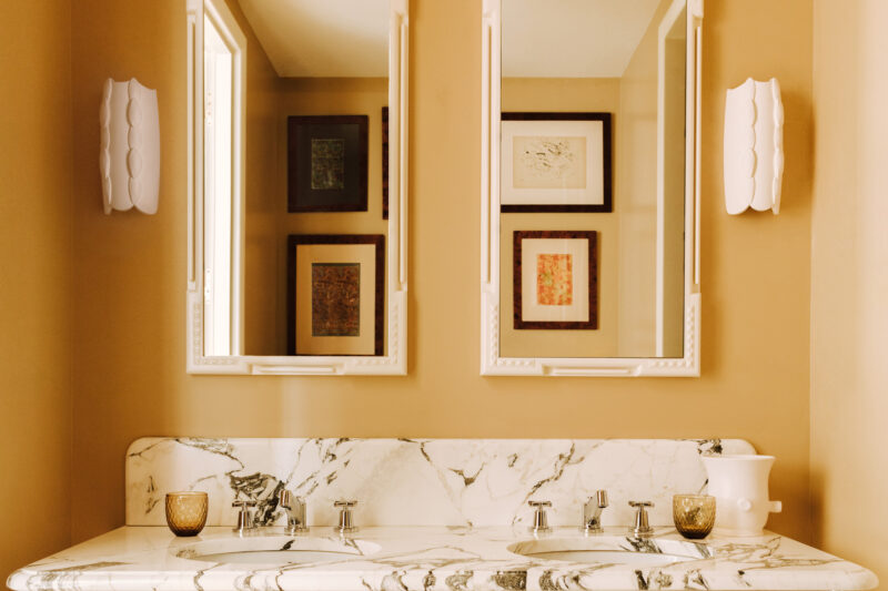 Elegant bathroom with a marble countertop, two mirrors, framed artwork, and decorative lighting.