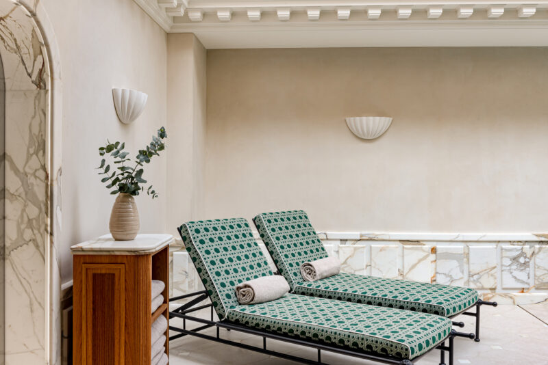 Wellness area at Saint James Paris featuring two green patterned loungers, a marble wall, and a decorative vase.