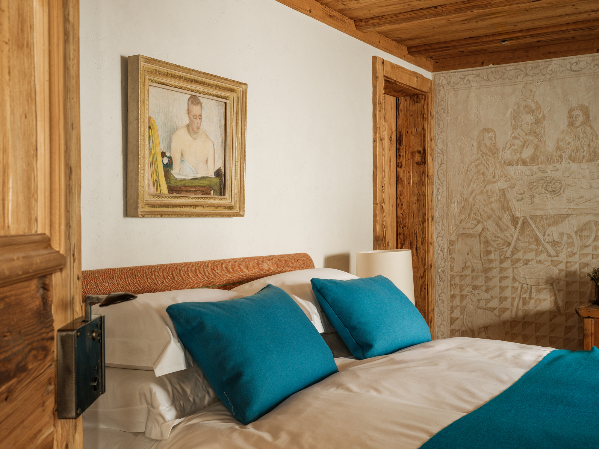 Cozy bedroom featuring a bed with turquoise pillows, a painting of a man, and textured wall decor.
